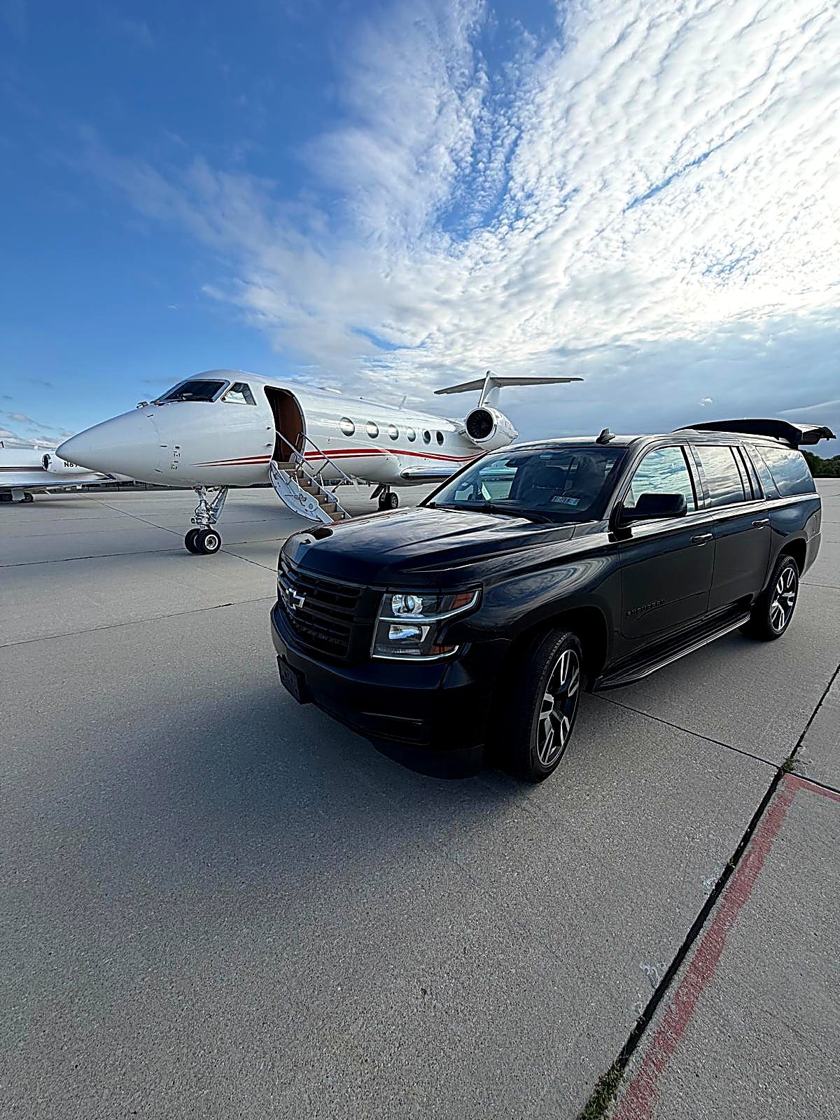 Black SUV facing the camera on an airport tarmac with a private jet behind it