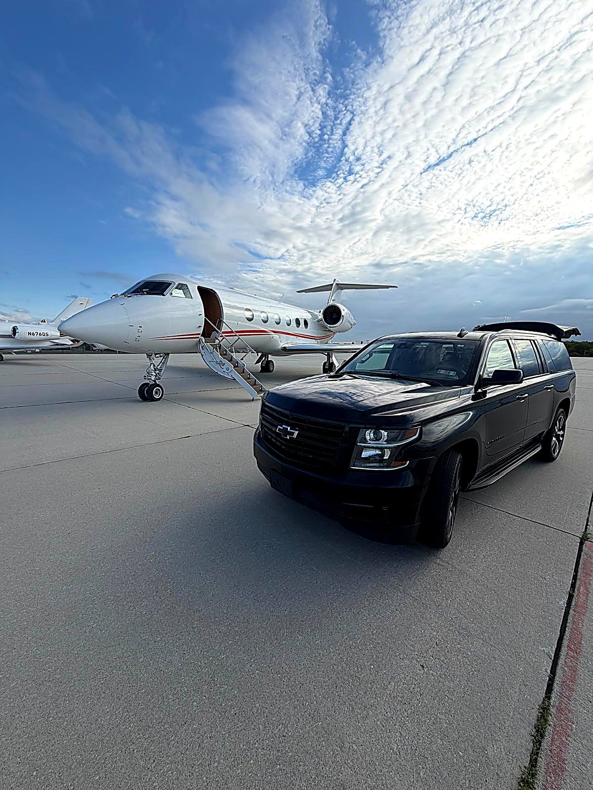 Black SUV on an airport tarmac beside a private jet with stairs down