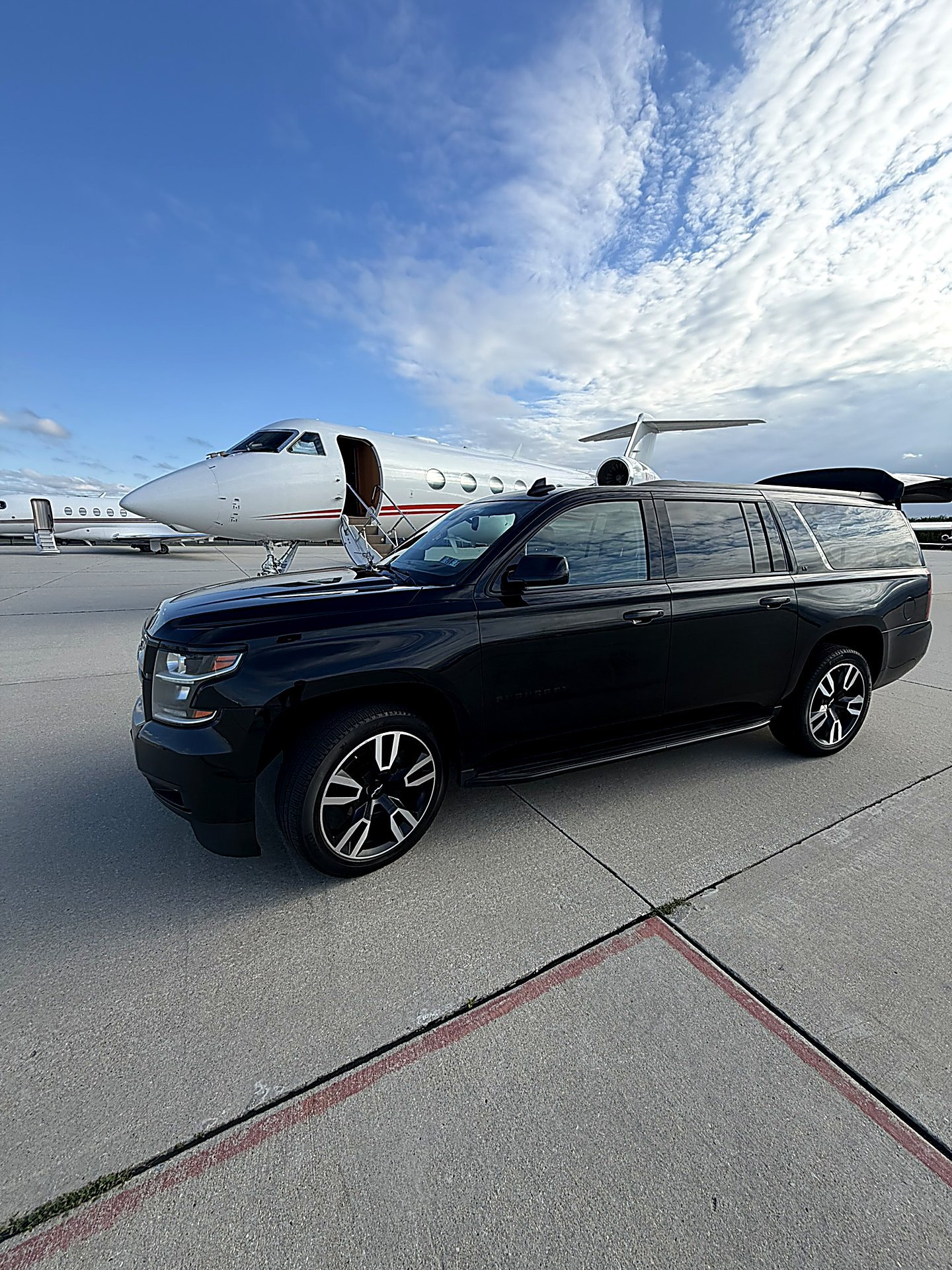 Black SUV parked on an airport tarmac in front of a private jet