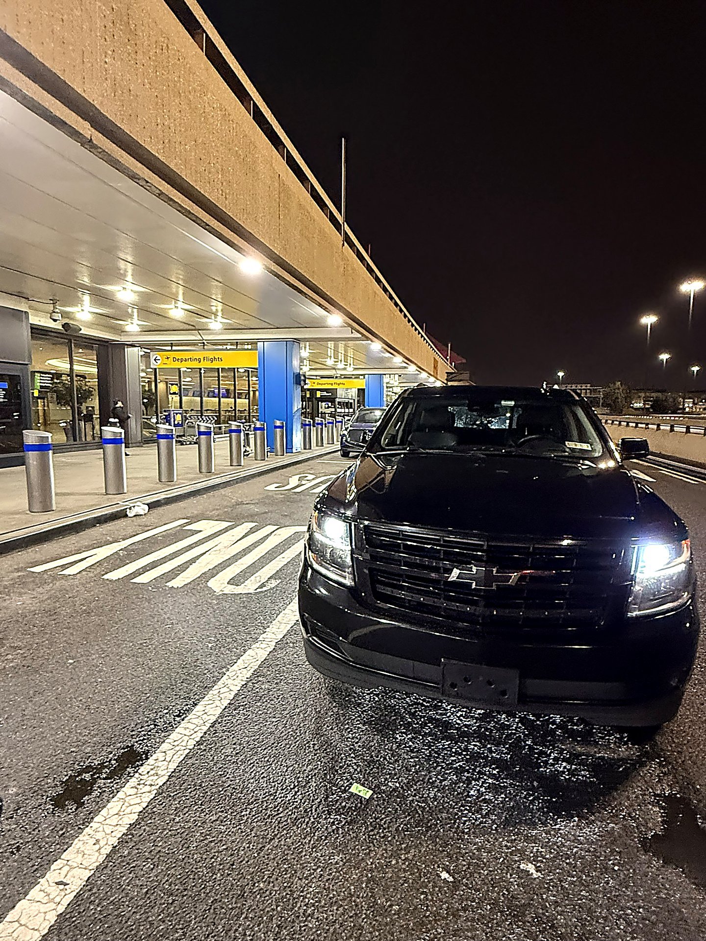Black SUV with headlights on outside an airport departures entrance at night