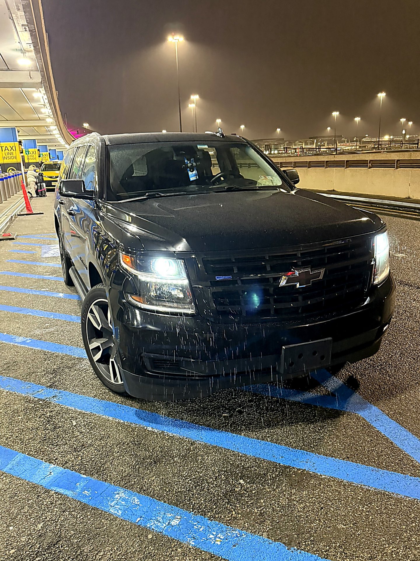 Black SUV with headlights on at an airport terminal curb at night