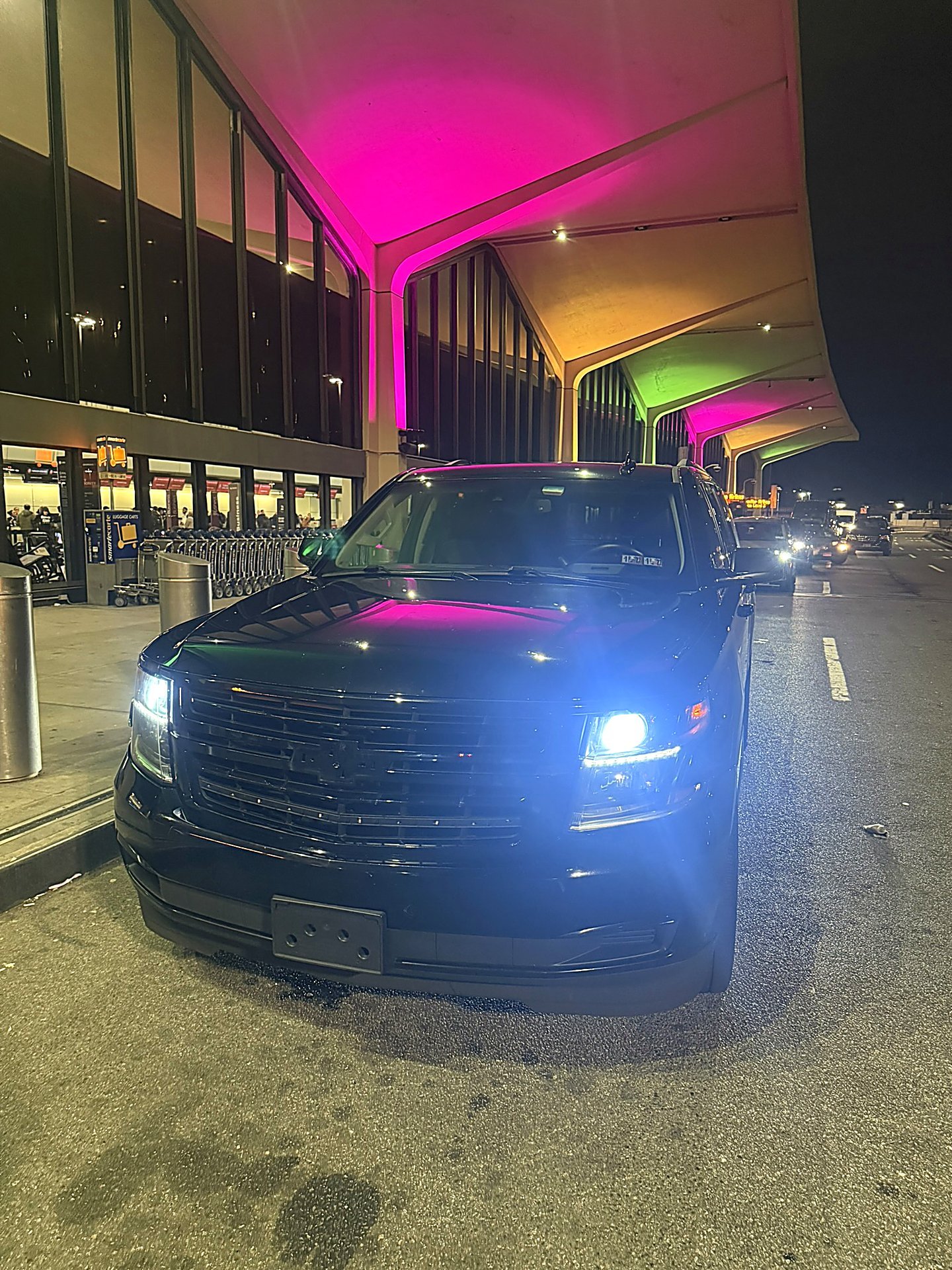 Black SUV under a brightly lit airport terminal canopy at night