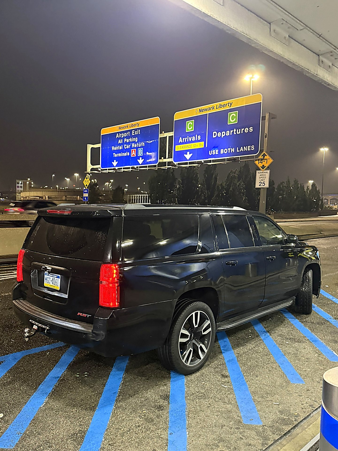 Black SUV parked at Newark Liberty airport arrivals and departures signs at night