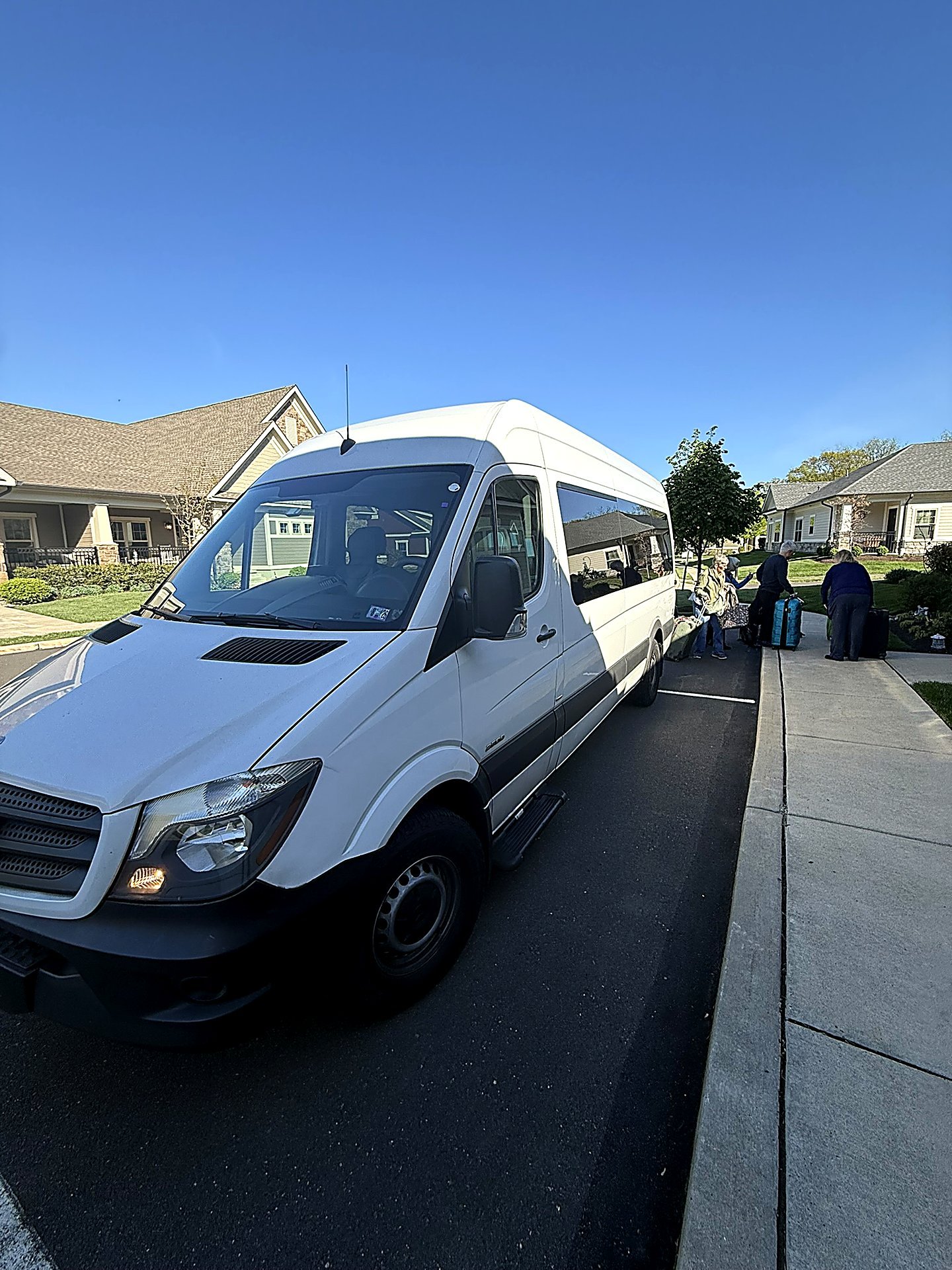 White Sprinter van parked on a street with passengers and luggage nearby