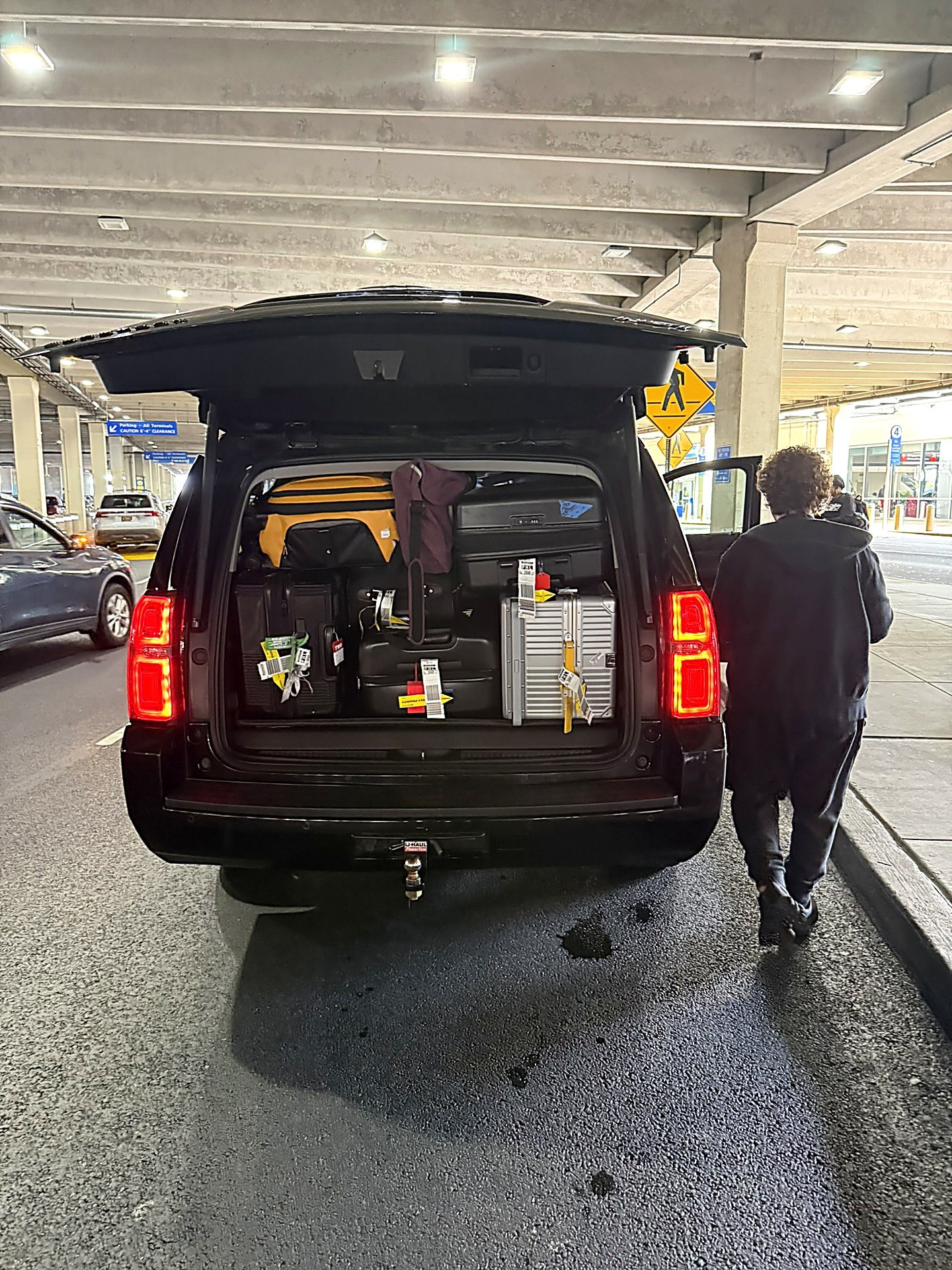 Chauffeur loading luggage into a black SUV at an airport terminal at night