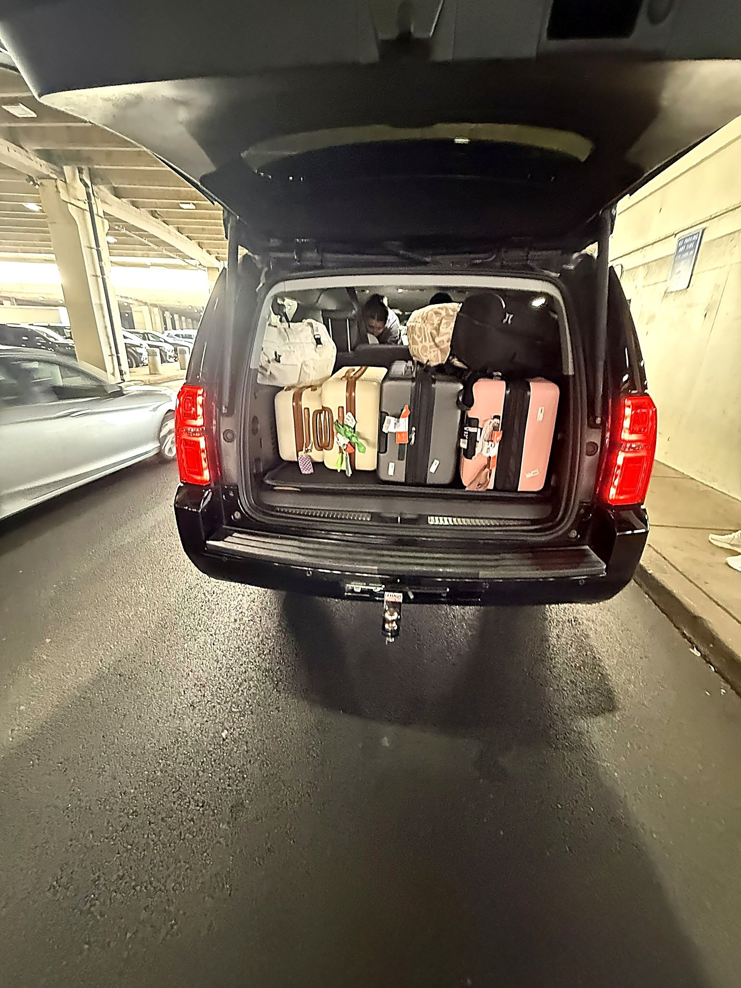 Black SUV trunk loaded with suitcases and bags in a parking garage