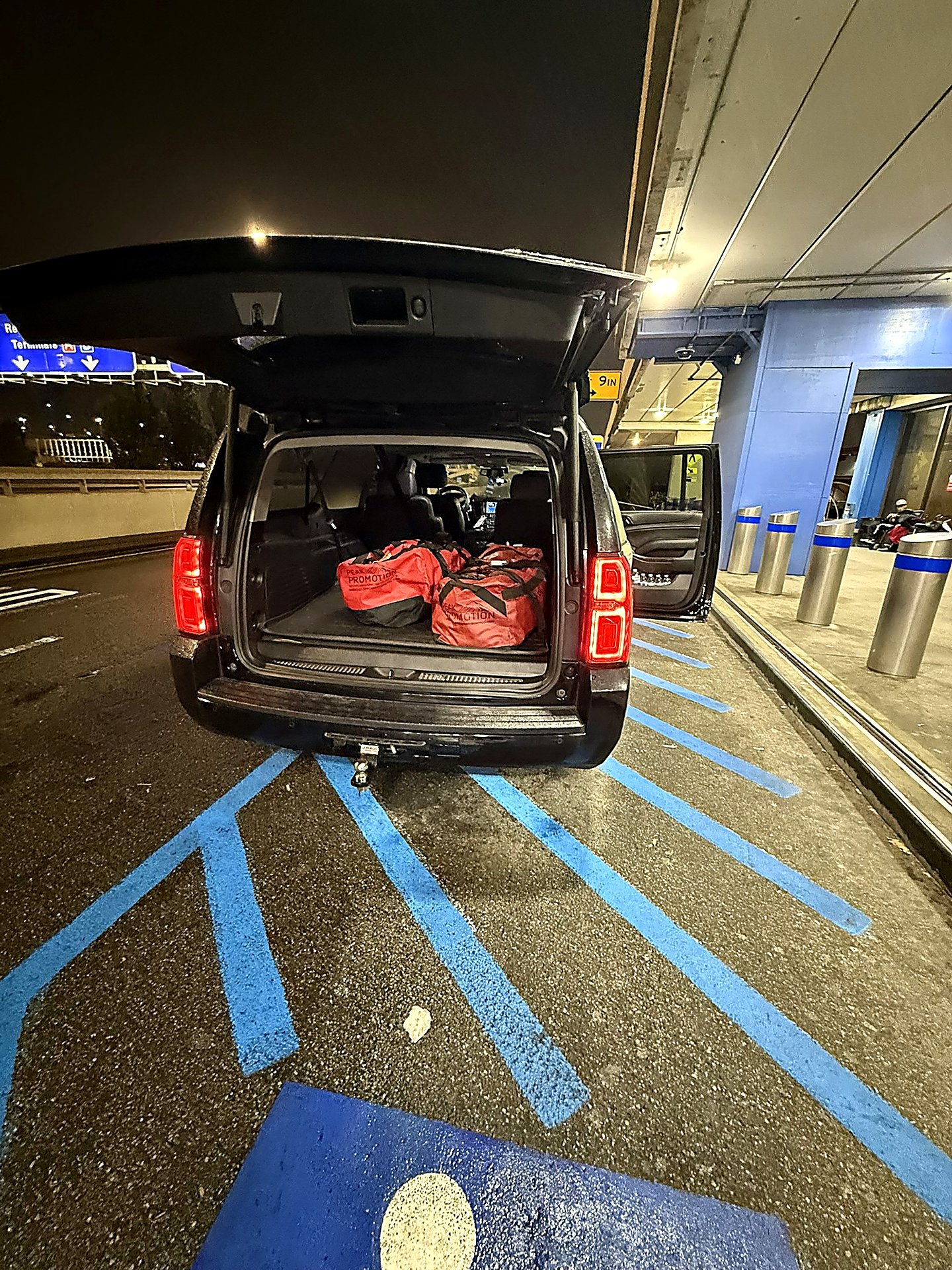 Black SUV at an airport curb at night with luggage in the open trunk