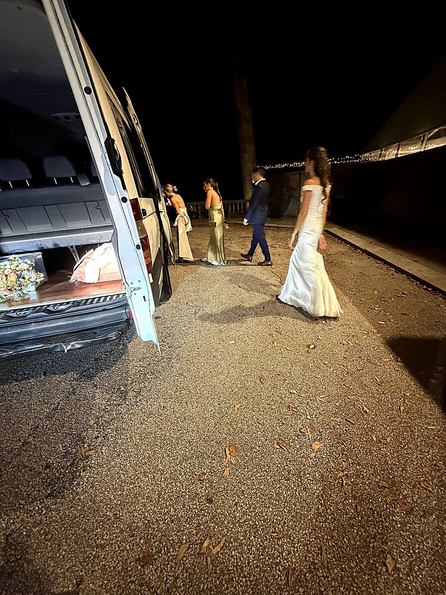Bride and wedding party walking to a white Sprinter van at night