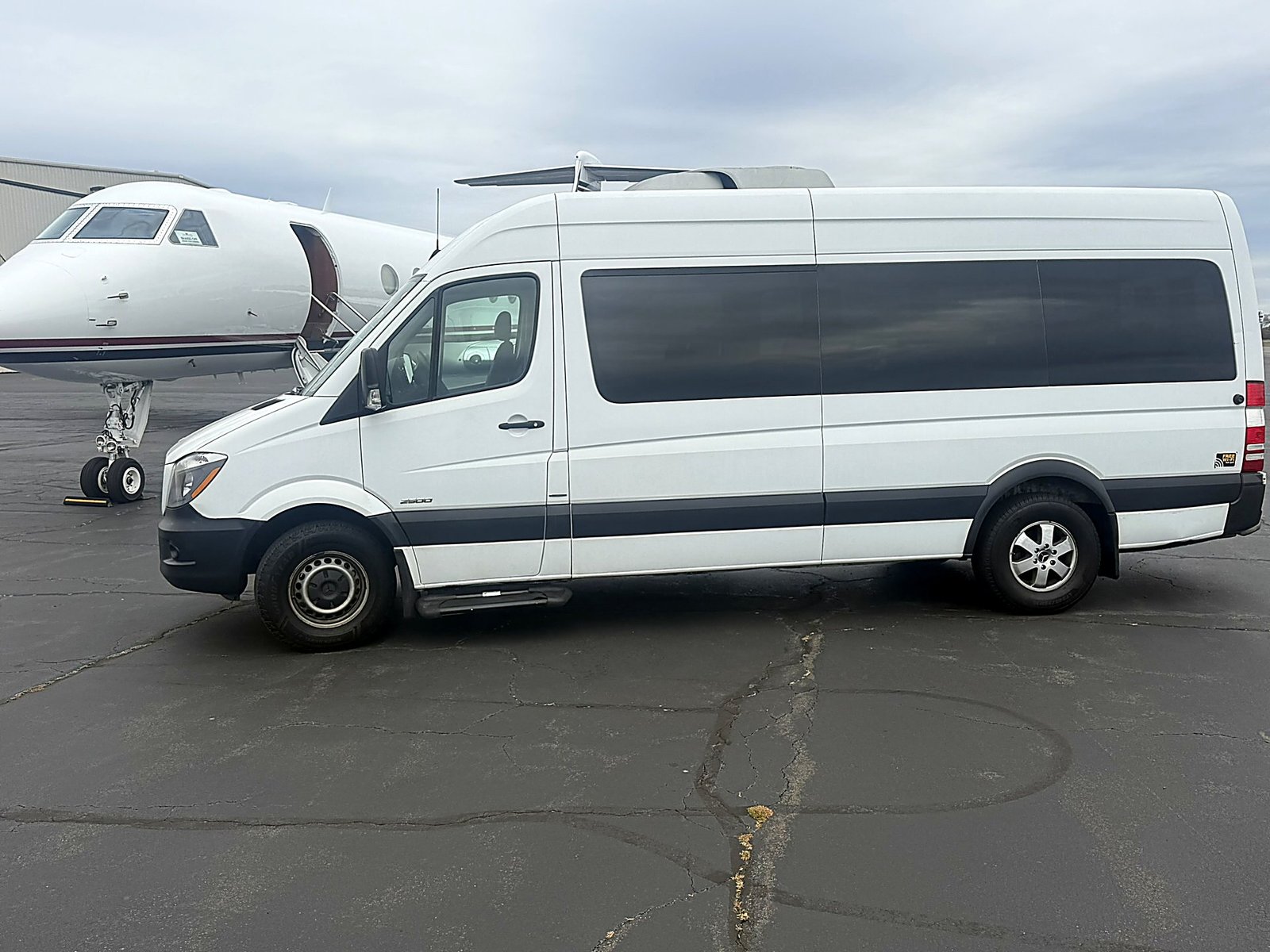 White Sprinter van beside a private jet